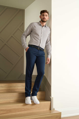 man standing on steps leaning against wall wearing navy blue chino-style pants and a button shirt
