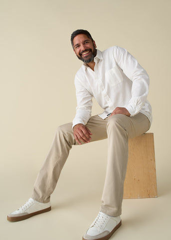 Tall man seated on box wearing khakis and a white button shirt