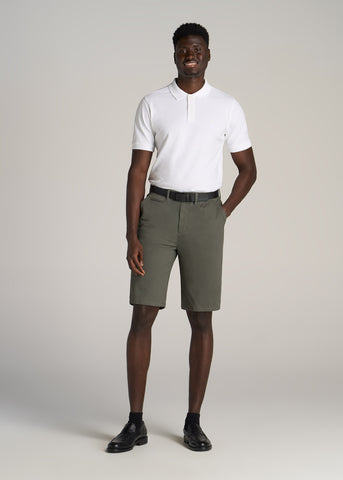 Man standing with. one hand in pocket wearing white polo tee and olive color chino shorts