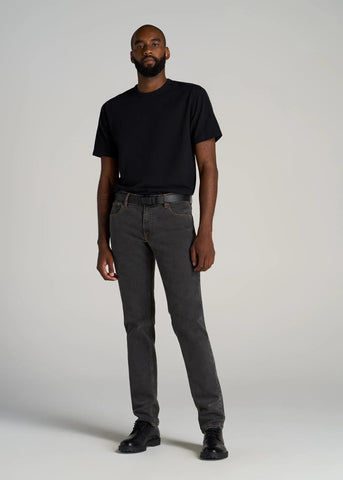 Tall slim man standing wearing black t-shirt tucked into black jeans