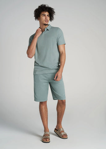 Tall man standing wearing green colored tall polo shirt with matching shorts