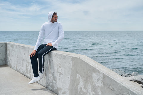 Tall man wearing athletic stripe pants and hoodie sitting by the lake